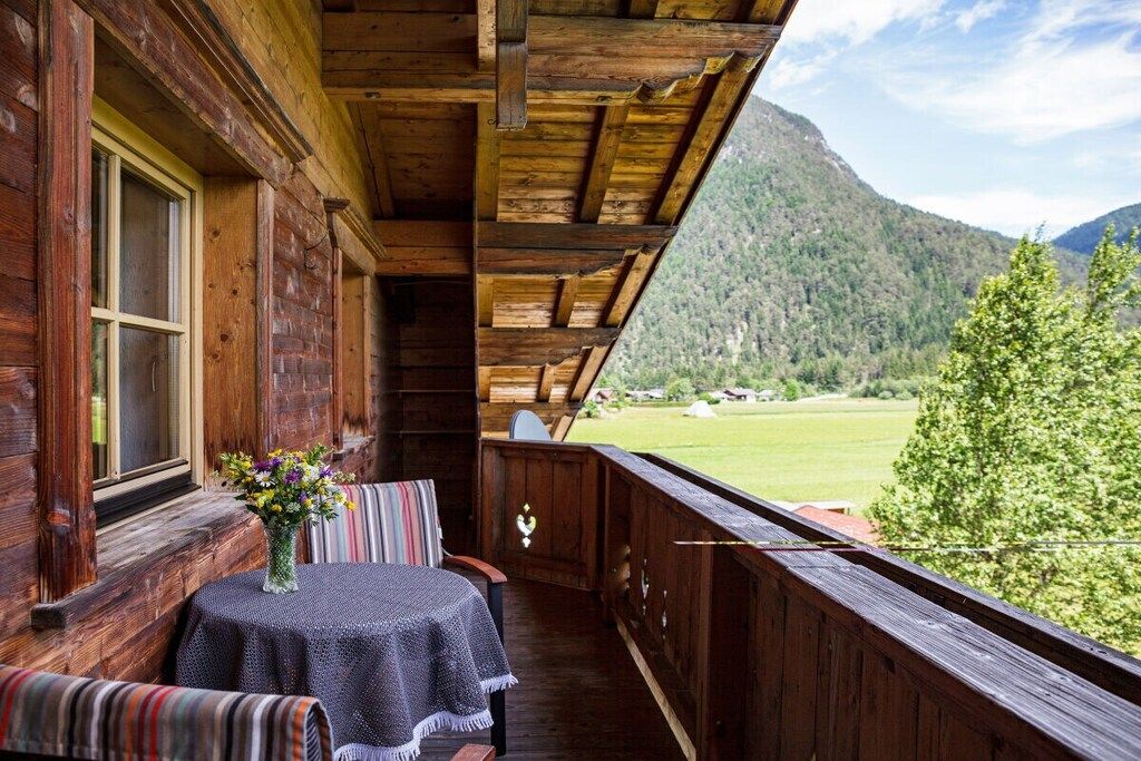 A wooden balcony with a table and chairs, overlooking a mountainous landscape.