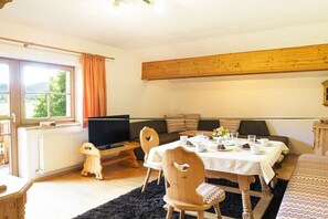 Ein gemütliches Wohnzimmer mit einem Holztisch, der für eine Mahlzeit gedeckt ist, einer Couch und einem Fernseher.