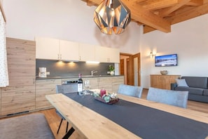 A modern kitchen with wooden cabinets, a dining table with a black tablecloth, and a pendant light. - Holiday apartment with 1 bedroom (Leogang, Österreich)