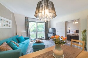 A modern living room with a sofa, a dining table, a chandelier, and a view of the outdoors. - Holiday apartment in Pirna with swimming pool (Pirna)