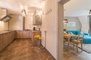 Cozinha moderna com armários de madeira, uma ilha central e um espaço de jantar com sofá azul e mesa de madeira.