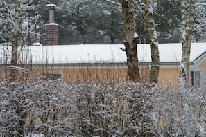 Schneebedeckte Landschaft mit einem Ziegelkamin und einem Gebäude mit gelber Fassade.