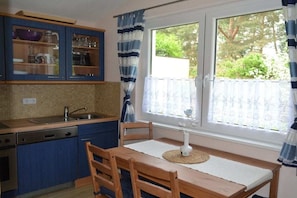 Eine Küche mit einem Holztisch und Stühlen, einem Fenster mit Vorhängen und Blick ins Grüne.