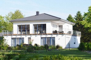 Ein zweistöckiges Haus mit großen Fenstern, einem Balkon und einem gepflegten Garten.