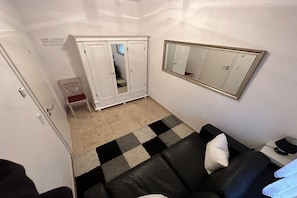 Ein Zimmer mit einer schwarzen Ledersofa, einem weißen Kleiderschrank, einem karierten Teppich und einem Spiegel an der Wand.