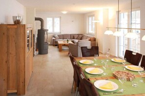 A cozy living room with a sofa, a dining table set for four, and a wood-burning stove. - Holiday home with 3 bedrooms (Glowe\/Rügen)
