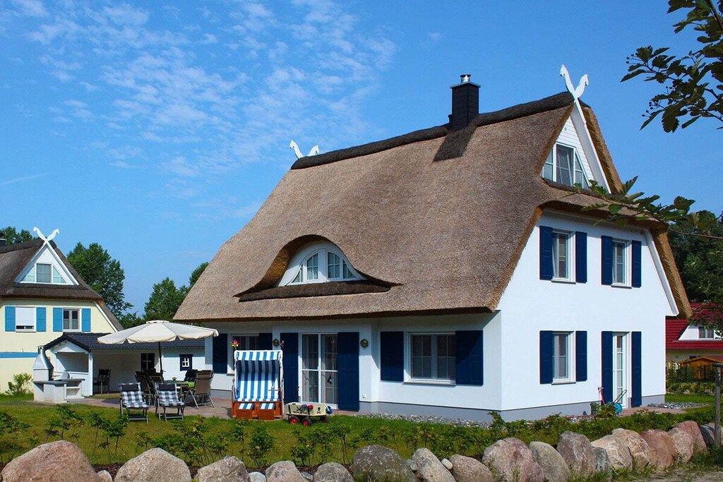 A house with a thatched roof, a porch with a striped awning, and a small garden area.