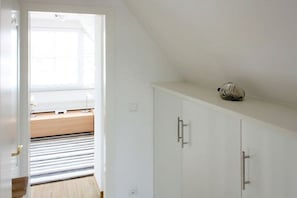 A room with a white wardrobe, a small shelf with a decorative item, and a window with blinds. - Holiday home with 3 bedrooms (Glowe\/Rügen)