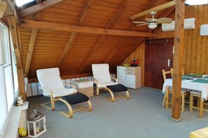 A cozy attic room with wooden beams, two white chairs, a small table, and a ceiling fan. - Holiday apartment with 2 bedrooms (Lübben)