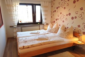 A bedroom with a bed, a window with curtains, a radiator, and a wall with floral wallpaper. - Holiday apartment with 2 bedrooms (Lübben)