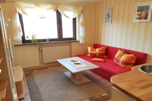 A cozy living room with a red sofa, a white coffee table, and a window with curtains. - Holiday apartment with 2 bedrooms (Lübben)