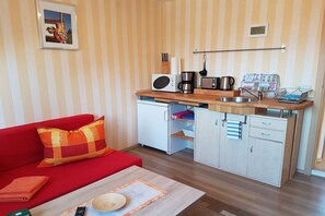 A compact living space with a kitchenette, a red sofa, and a small dining table. - Holiday apartment with 2 bedrooms (Lübben)