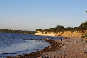 Eine Küstenlandschaft mit steinigem Strand, ruhigem Wasser und einer Klippe mit Vegetation.