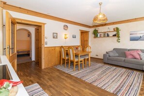 Ein Zimmer mit einem Holzespeisetisch, Stühlen, einem grauen Sofa und einem gemusterten Teppich.
