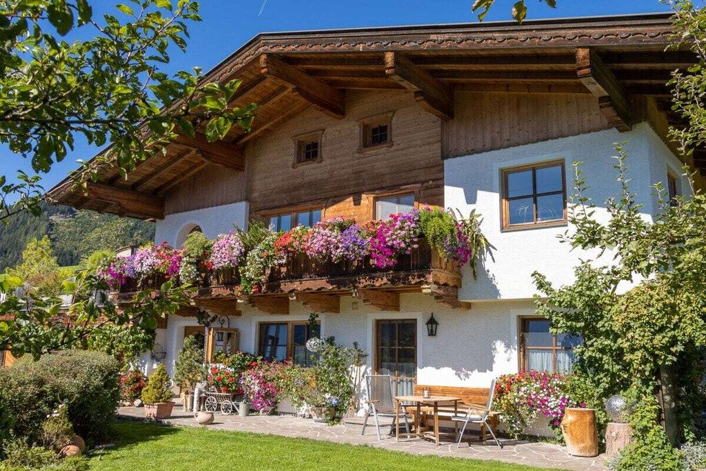 Een traditionele chalet met een houten balkon, een stenen terras en een tuin met bloempotten.
