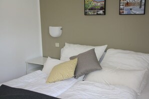 A bed with white bedding and two pillows, a bedside table, and a wall-mounted light fixture. - Holiday apartment in Waren with swimming pool (Waren)