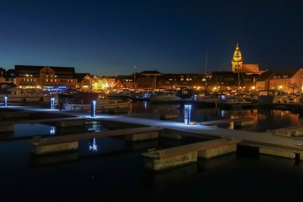 Una zona sul lungomare con edifici, una torre imponente e un porto turistico con barche.