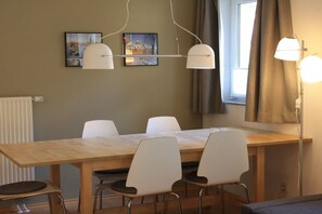 A dining area with a wooden table and white chairs, a hanging light fixture, and two framed pictures on the wall. - Holiday apartment in Waren with swimming pool (Waren)