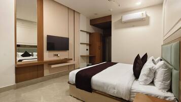 Habitación de hotel moderna con cama, televisor de pantalla plana, ventilador de techo y espacio de almacenamiento integrado.