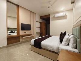 Habitación de hotel moderna con cama, televisor de pantalla plana, ventilador de techo y espacio de almacenamiento integrado.