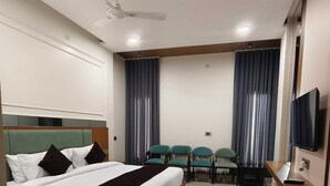 A hotel room with a bed, a desk, a chair, a television, and a ceiling fan. - Hotel Royal DC (Aligarh)
