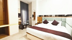 A hotel room with a large bed, a desk, a chair, a television, and a mirror. - Hotel Royal DC (Aligarh)