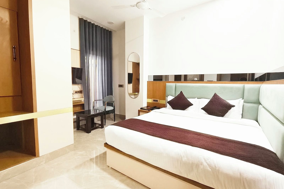 A hotel room with a large bed, a desk, a chair, a television, and a mirror.