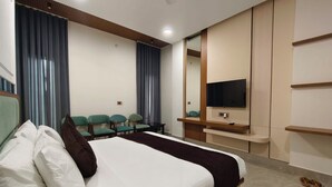 A hotel room with a bed, a TV, a seating area with chairs, and a mirror. - Hotel Royal DC (Aligarh)
