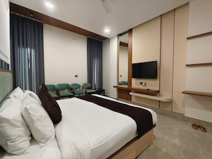 A hotel room with a bed, a TV, a seating area with chairs, and a mirror. - Hotel Royal DC (Aligarh)