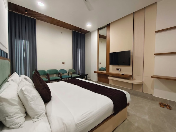 A hotel room with a bed, a TV, a seating area with chairs, and a mirror.