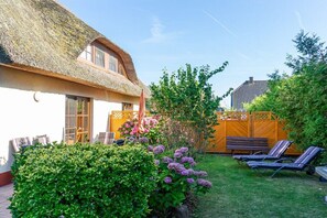 A thatched-roof house with a garden, a wooden fence, and lounge chairs. - Holiday home in Glowe with swimming pool (Glowe)