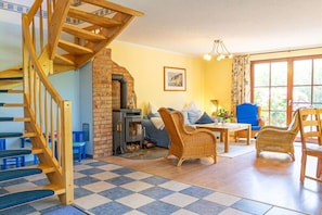 A cozy living room with a wooden staircase, a fireplace, a sofa, and wicker chairs. - Holiday home in Glowe with swimming pool (Glowe)