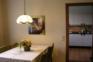 Zona de menjador amb una taula preparada per a dues persones, un ram de flors i un quadre a la paret.
