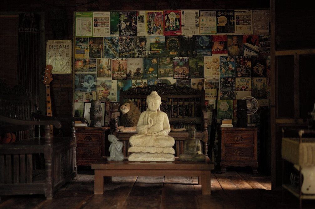 A room with a wooden bench, a statue, and a wall covered with various posters and books.