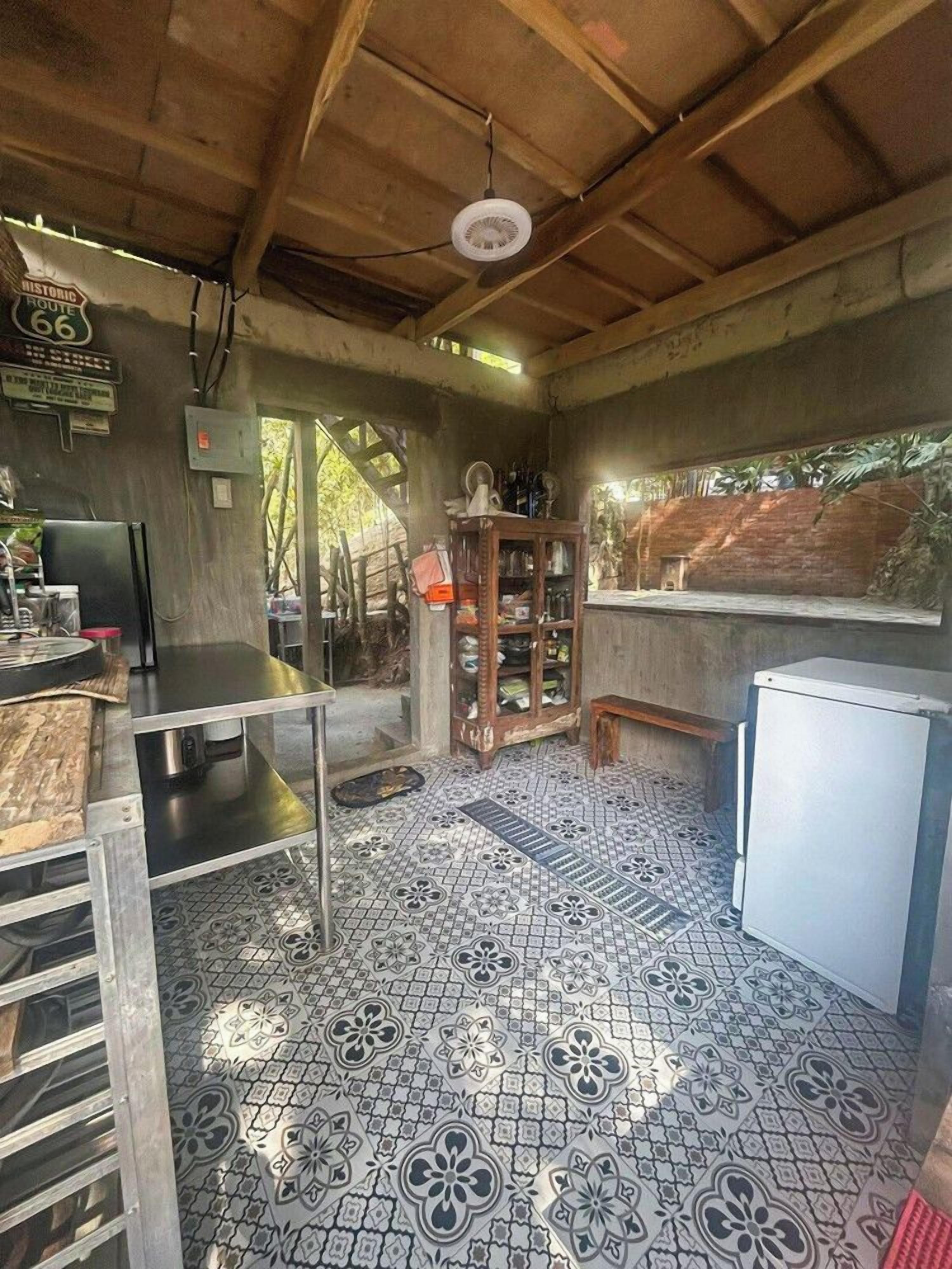 A rustic kitchen with a tiled floor, a wooden ceiling, and a refrigerator.