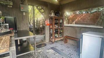 A rustic kitchen with a tiled floor, a wooden ceiling, and a refrigerator.