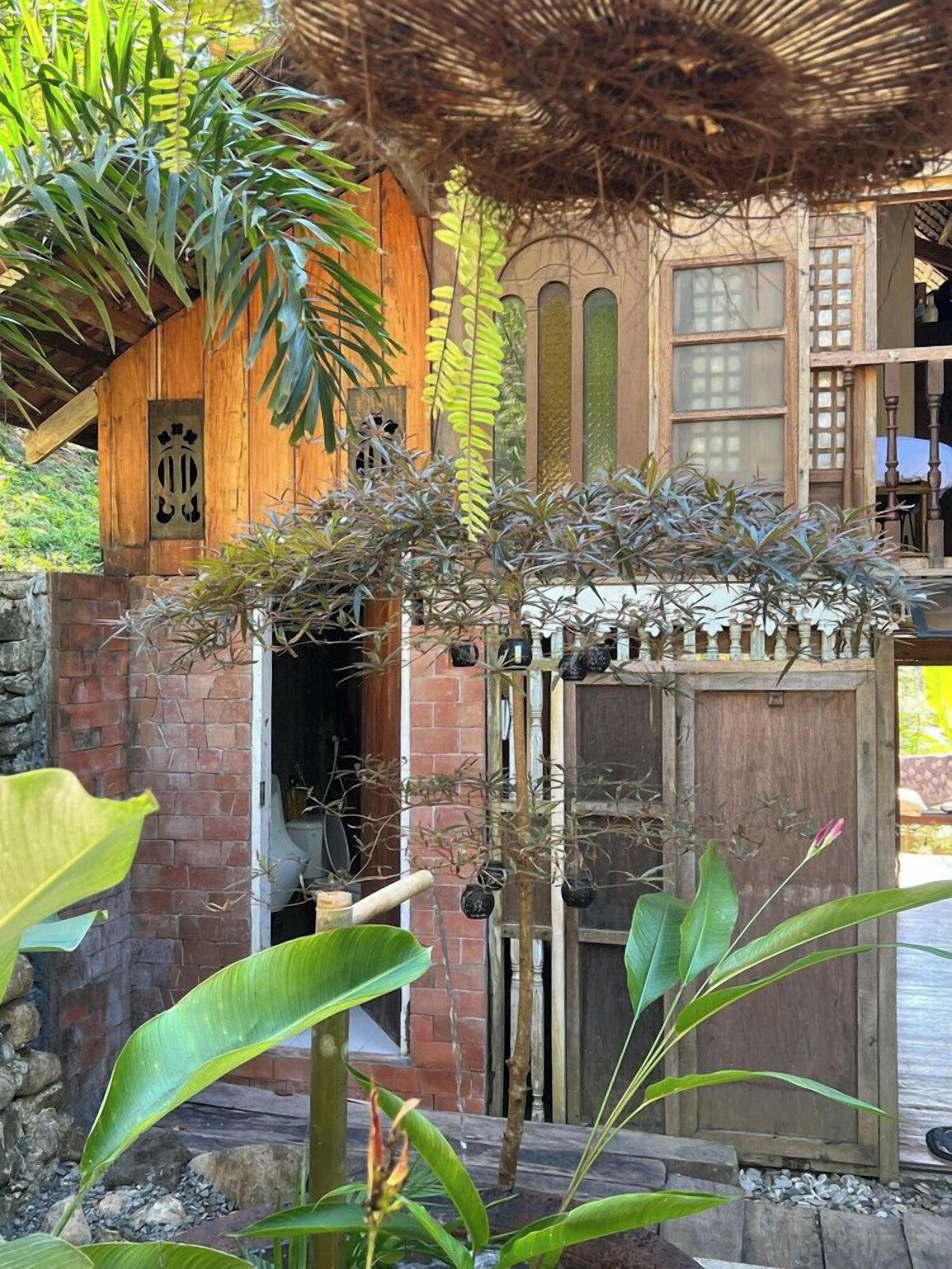 A wooden structure with a thatched roof, a brick wall, and a wooden door with a decorative design.
