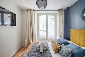 A bedroom with a bed, a window with curtains, a television on the wall, and a hanging light fixture. - Elegant Apartment with AC - Center of Paris (Paris)