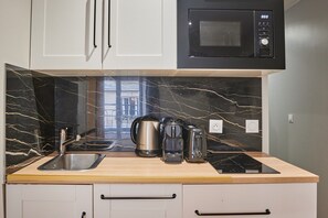 A modern kitchen with a black microwave, stainless steel kettle, and coffee maker on the counter. - Elegant Apartment with AC - Center of Paris (Paris)