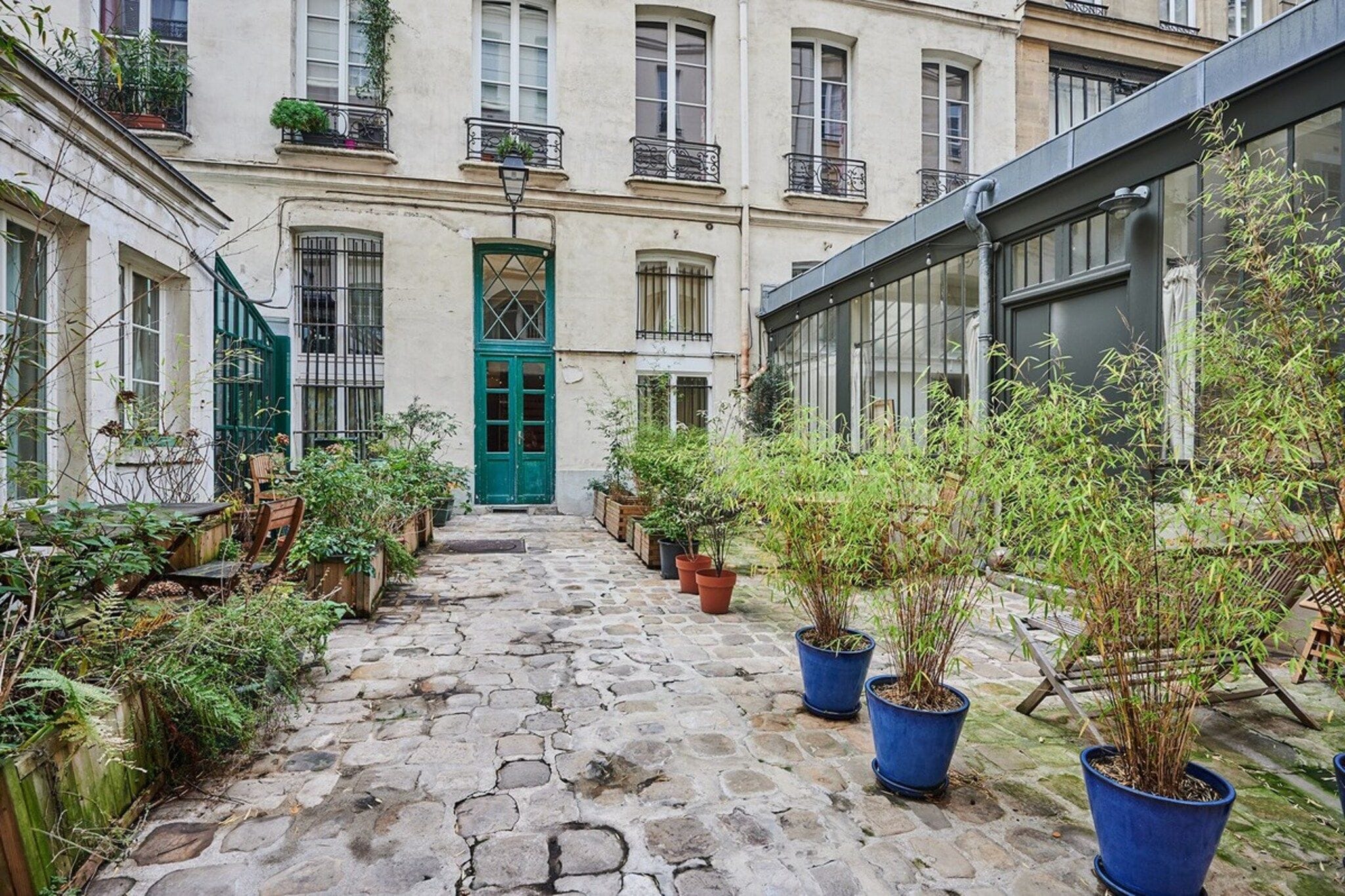 A narrow cobblestone alley with potted plants and wooden benches.