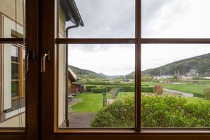 A view through a window of a countryside landscape with a building, a grassy area, and hills in the distance. - Holiday apartment with 2 bedrooms (Bad Schandau)
