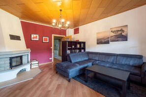 A living room with a fireplace, a sectional sofa, a coffee table, a bookshelf, and a chandelier. - Holiday apartment with 2 bedrooms (Bad Schandau)