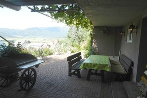 An outdoor patio with a table and benches, a cart, and a view of a village and mountains. - Holiday apartment with 1 bedroom (Mariapfarr)