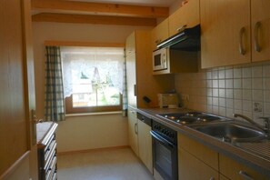 A compact kitchen with wooden cabinets, a microwave, a dishwasher, and a window with curtains. - Holiday apartment with 1 bedroom (Mariapfarr)