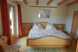 A bedroom with a wooden bed, a chair, a window with curtains, and a painting on the wall. - Holiday apartment with 1 bedroom (Mariapfarr)