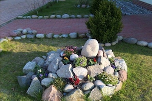 A garden with a central rock formation surrounded by various plants and flowers. - Holiday home in Glowe with swimming pool (Glowe)