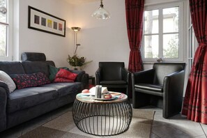 A living room with a sofa, two armchairs, a round coffee table, a floor lamp, and a framed picture on the wall. - Holiday home in Glowe with swimming pool (Glowe)