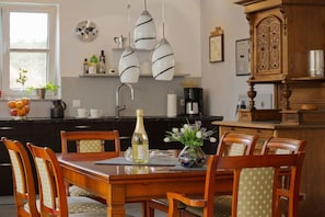 A dining area with a wooden table and chairs, a vase with flowers, and a bottle of wine. - Holiday home in Glowe with swimming pool (Glowe)