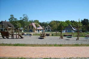 A playground with swings and a slide, surrounded by houses with red roofs. - Holiday home in Glowe with swimming pool (Glowe)