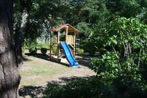 A wooden play structure with a slide in a garden setting. - Holiday home in Glowe with swimming pool (Glowe)